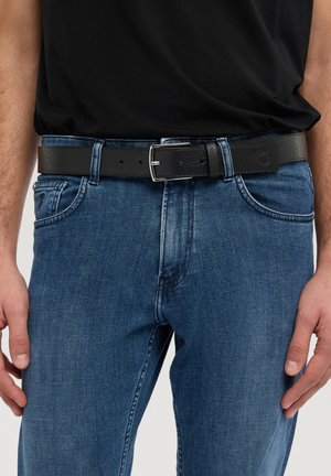 Czarny skórzany pasek o fakturowanej powierzchni, z srebrną metalową klamrą i pięcioma otworami do regulacji, noszony z niebieskimi dżinsami.