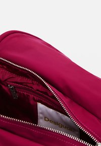 Borsa con zip fucsia in tessuto liscio, caratterizzata da una zip argentata e tasche interne. Include un'etichetta con la scritta "Desigual."
