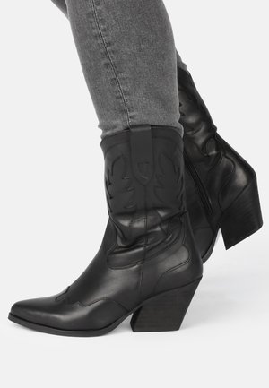Botas de vaquero de cuero negro con punta afilada, costuras decorativas y un tacón ancho medio. Presentan un zipper lateral para facilitar su uso.