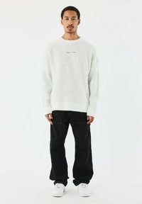 Witte, fluffy trui met ribbelmanchetten, gecombineerd met zwarte cargobroeken met ritssluitingen en witte sneakers. Eenvoudig ontwerp, minimale details.
