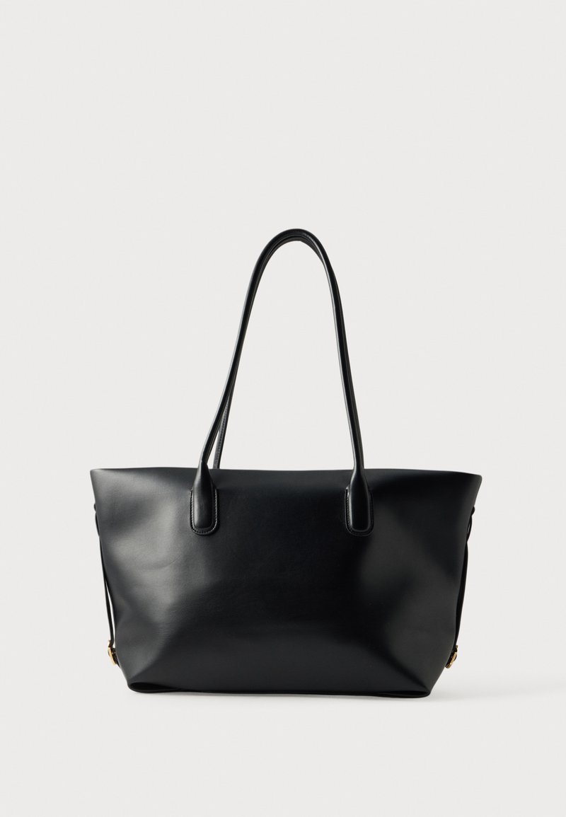 Sac cabas en cuir noir avec deux longues anses et une surface lisse et unie, présenté sur un fond clair uniforme.