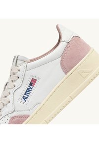 Sneakers in pelle bianca con dettagli in camoscio rosa. Presentano una suola texturizzata, chiusura con lacci e una piccola toppa con logo della bandiera americana.
