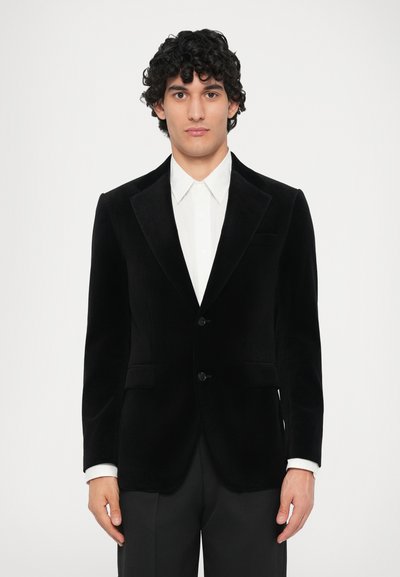 Black velvet blazer with a notched lapel, lightweight texture, single-button closure, and two front pockets, worn over a white shirt.