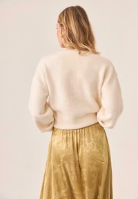 Suéter de punto color crema con un corte relajado y hombros caídos, combinado con una falda dorada fluida y con estampado.