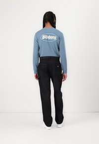 Plava long sleeve košulja s "Billabong" logotipom na leđima, u kombinaciji s crnim cargo hlačama. Ima džepove i ležeran kroj.
