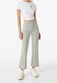 Jasnoszare spódnice dzwony wykonane z teksturowanej tkaniny, z wysokim stanem i kieszeniami po bokach, zestawione z dopasowanym białym topem crop oraz białymi trampkami.