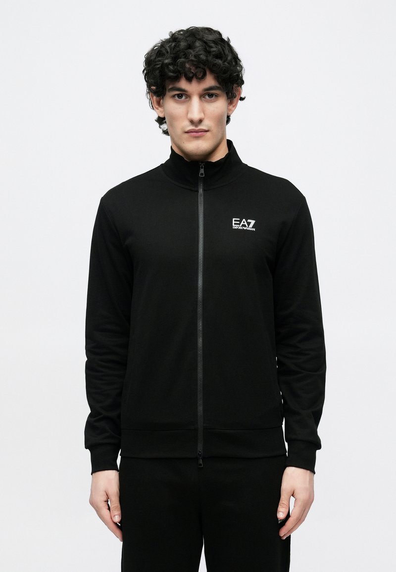 Μαύρο μπουφάν με φερμουάρ, κατασκευασμένο από λείο ύφασμα, με ψηλό γιακά και λογότυπο EA7 στο αριστερό στήθος. Μακριά μανίκια με ριμπ μανσέτες.