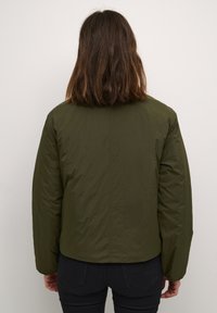 Oliivroheline puffjakker, millel on tekstuuriga viimistlus, ümmargune kaelus ja pikad varrukad. Seljaosa on sile ja kitsas siluett.