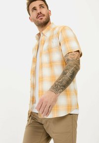 Korte mouwen, geel en wit geruit shirt met een button-down kraag, gemaakt van lichte stof, gedragen over een wit t-shirt.
