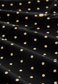 Tela negra con una textura suave, que presenta puntos de lunares crema distribuidos uniformemente. El material parece ligero y flexible, con ligeros pliegues.