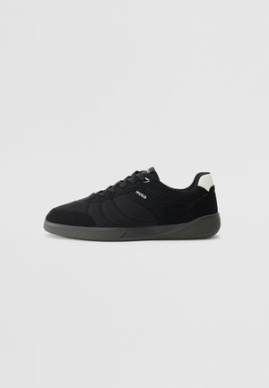 Black athletic shoes featuring a mix of materials, including mesh and suede, with a textured sole and contrasting white heel accent.