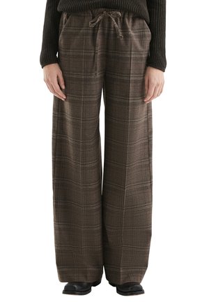Pantalon marron à carreaux à jambes larges avec poches avant et taille à cordon, porté avec des bottes noires et un pull en maille noir.