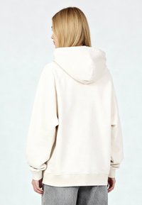 Felpa con cappuccio color crema in tessuto morbido; presenta un ampio cappuccio, polsini a coste e una vestibilità morbida con una texture uniforme.