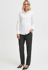 Witte button-down shirt, zwarte pinstriped broek, en zwarte hakken. Gladde stof, op maat gemaakt pasvorm, en scherp kraagontwerp.