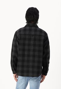 Chemise en flanelle à carreaux noir et gris, avec un col, des poignets à boutons et un détail de empiècement au dos, associée à un jean en denim bleu clair.