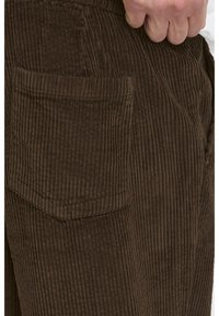Brown corduroy pants with a ribbed texture, featuring a single patch pocket on the back, highlighting utility and durability.