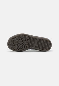 Semelle en caoutchouc gris de sneaker avec un motif texturé comprenant des détails circulaires et triangulaires, étiquetée "adidas" sur le côté.