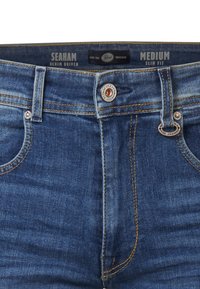 Vaqueros ajustados de corte medio en denim azul oscuro con costuras doradas, herrajes de botones metálicos y un clásico diseño de cinco bolsillos.