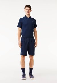 Navy blue polo shirt with short sleeves, featuring a green logo, paired with matching navy shorts. Soft fabric with a relaxed fit.