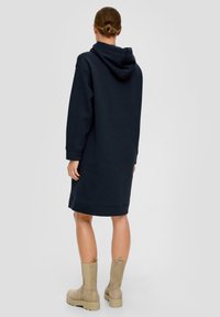 Marinblå hoodieklänning med avslappnad passform, långa ärmar och en känguruficka. Matchad med beige ankellåga stövlar och en slät textur.