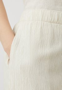 Tissu texturé de couleur crème présentant un motif froissé, avec une taille élastique et des poches latérales.