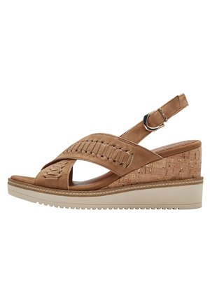 Sandalo con zeppa in suede tan, con base in sughero, caratterizzato da cinturini incrociati e dettagli intrecciati, una cinghia regolabile alla caviglia e una suola testurizzata.