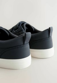 Marineblauwe sneakers met textiel, witte rubberen zolen, gewatteerde kraag en kleine trekplanken aan de achterkant, met een strak ontwerp.