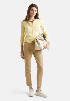 Cárdigan amarillo claro con botones, pantalones ajustados beige y zapatillas blancas. Sosteniendo un bolso estampado con acentos florales.