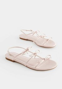 Lyserøde flade sandaler med flere tynde stropper og sløjfer, der har en glat syntetisk overdel og en minimalistisk gummisål.