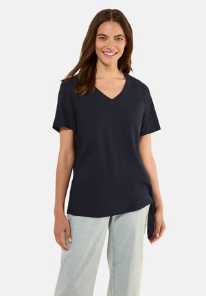 T-shirt V en jersey marine à manches courtes, tissu doux, coupe ample et détail à nouer sur le côté. Associé à un jean large bleu clair.