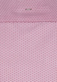 Reversible stof in roze met witte diamantenpatronen, gladde textuur, met een klein metallic label bovenaan.