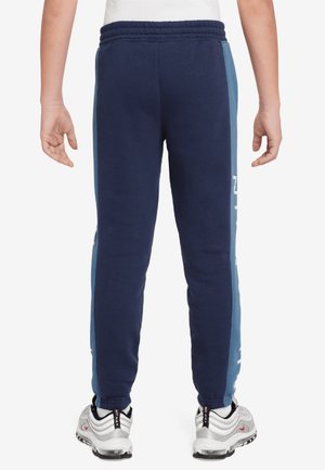 Marineblauwe joggingbroek met blauwe zijpanelen, elastische tailleband en witte tekstdetails op het linkerbeen. De stof lijkt zacht en rekbaar.