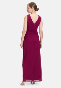 Dlhé bezrukávové šaty s hlbokým V-výstrihom z bordovej látky. Obsahujú nariasenie v oblasti pása a skrytý zips na chrbte.