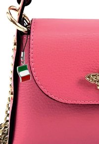 Roze faux leren handtas met een gouden kettinghengsel, met een metalen vlinderaccent en een klein Italiaans vlaggetje als bedel.
