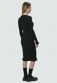 Vestido de punto negro acanalado con mangas largas y dobladillo con ondas, combinado con calcetas hasta la rodilla a juego y zapatos negros gruesos.