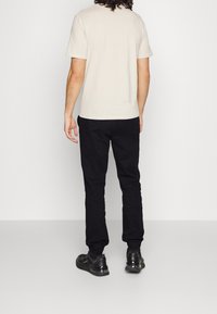 Maglietta beige a maniche corte abbinata a pantaloni neri a sigaretta. L'outfit presenta un design semplice senza motivi o accenti visibili.