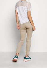 Camiseta blanca con mangas de encaje y espalda, combinada con jeans beige claros y zapatillas color teal, mostrando un diseño ajustado y un estilo casual.