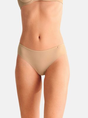 Vrouw draagt naadloos beige ondergoedsetje, waarbij de buik en bovenbenen zichtbaar zijn tegen een effen lichte achtergrond.