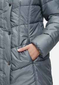 Manteau en duvet gris avec texture matelassée, fermeture à boutons et poches latérales, présentant une finition lisse et brillante ainsi que des manches volumineuses.