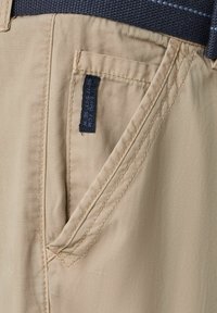 Beige stoffen shorts met een voorzak en zichtbare stiksels. Heeft een donkere stoffen tailleband met een geweven textuur.