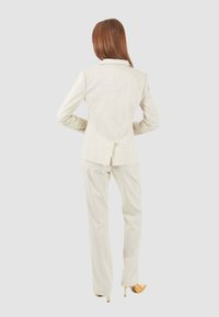 Completo beige chiaro su misura con giacca aderente e pantaloni dritti. Tessuto liscio, caratterizzato da sottili righe verticali.