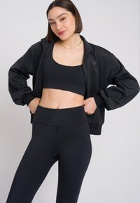Completo sportivo nero caratterizzato da un top corto e leggings a vita alta, realizzati in materiale liscio e elasticizzato con un design aderente.