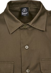 Camisa marrón de manga corta en tejido suave con un gran cuello, dos bolsillos frontales y cuatro botones con un ligero brillo.