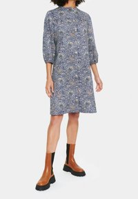 Blå paisleymönstrad klänning med långa ärmar, knäppning fram och en avslappnad passform, ihop med bruna ankellånga stövlar med en kraftig sula.