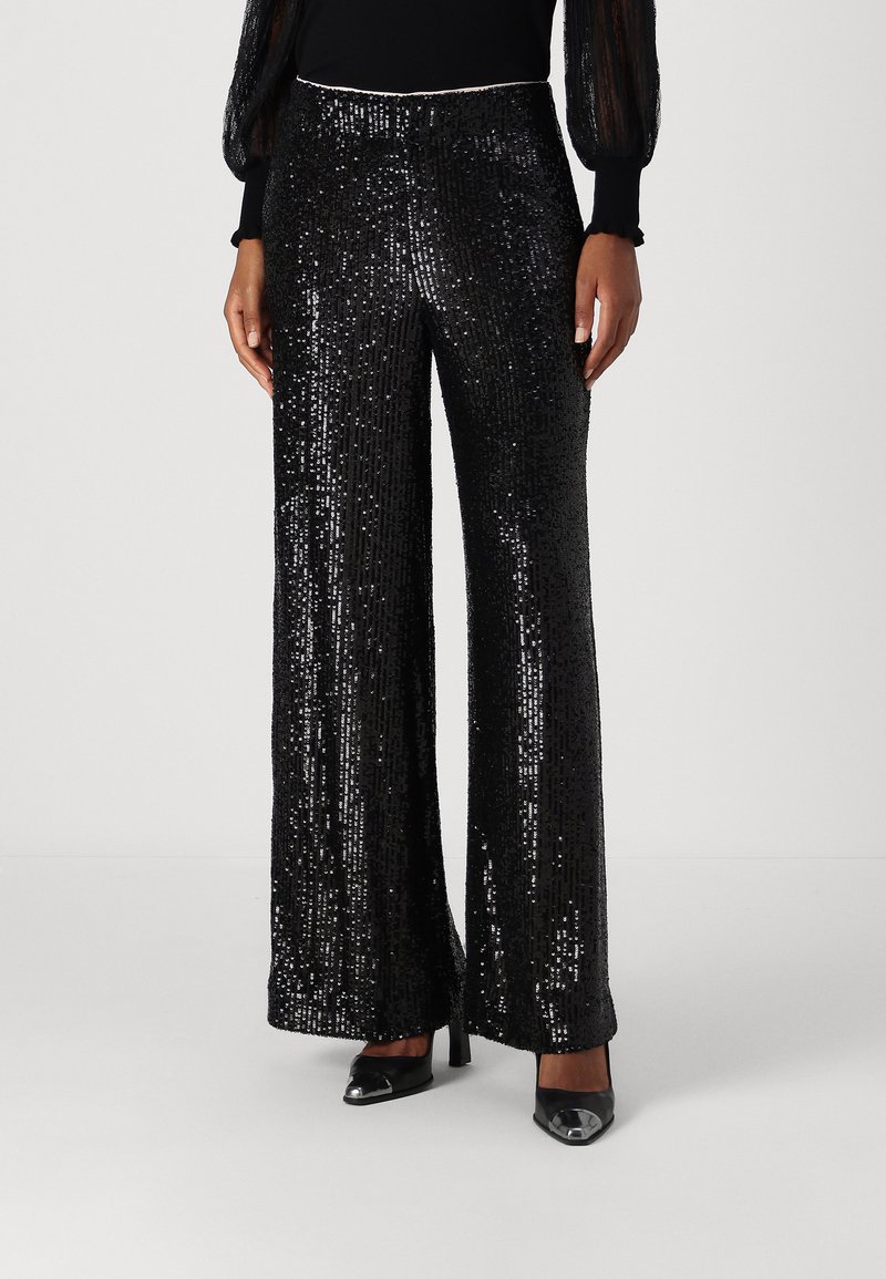Black sequin pants featuring a wide leg design, glossy finish, and a fitted waistband, paired with black high heels.