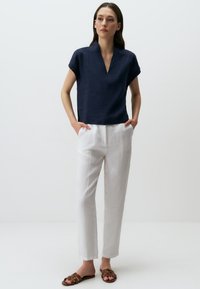 Haut en lin navy avec un col en V et des manches courtes, assorti à un pantalon en lin blanc et des sandales plates marron. Design simple, texture légère.