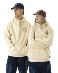 Beige hettegenser med frontlomme, med en logo i oransje. Mørke denimjeans med et subtilt mønster. Brun kordfløyelscaps på en modell.