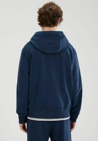 Felpa con cappuccio blu navy dal fit rilassato, texture morbida e polsini a costine. Presenta un ampio cappuccio sul retro e dettagli di cucitura minimali.