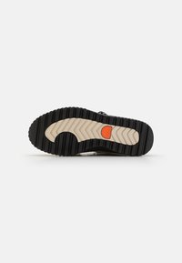 Svar på svart og beige skosåle med zigzag mønster, oransje aksent og teksturert gummioverflate for bedre grep og holdbarhet.