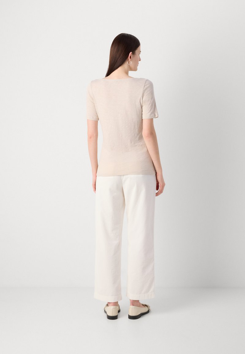 Beige Oberteil mit kurzen Ärmeln, kombiniert mit weißen, weit geschnittenen Hosen. Das Outfit zeichnet sich durch ein einfaches Design und eine weiche Textur aus.